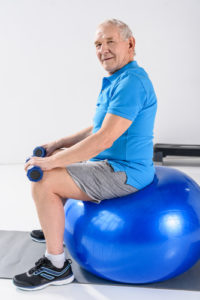 Senior on exercise ball with hand weights