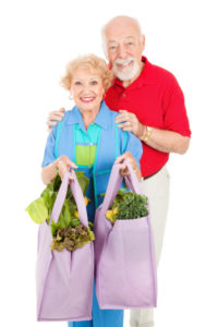 Senior couple using reusable shopping bags to bring home their groceries. Isolated on white.